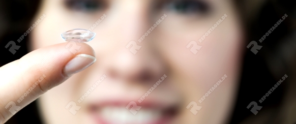 Closeup of a face of a woman with a contact lense on her finger